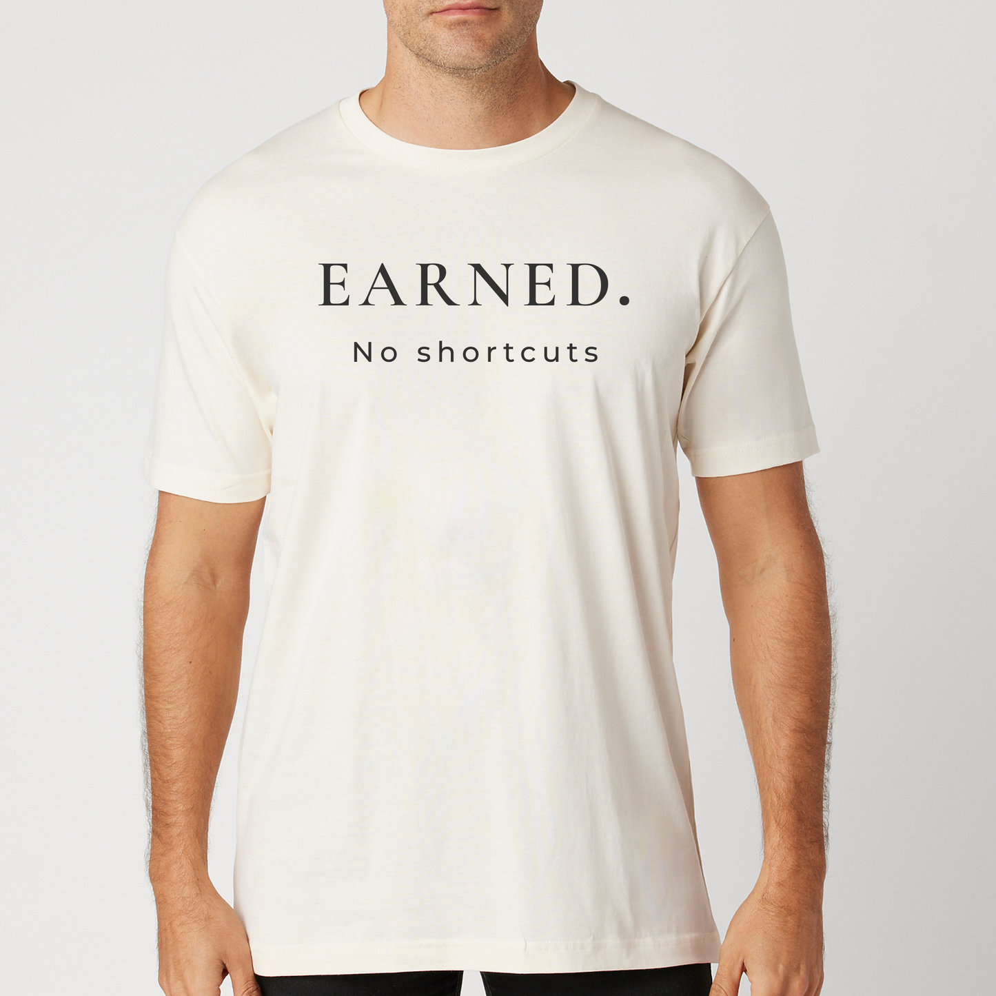 Person wearing a vintage white t-shirt with 'Earned. No shortcuts.' text on a plain background